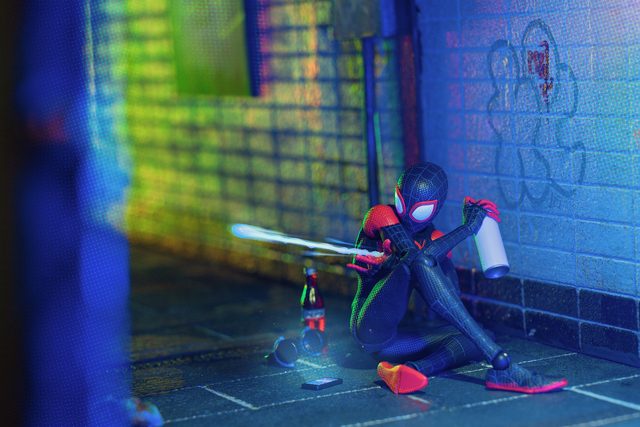 A Spider-Man figure sitting against a tiled wall, spray-painting it in neon light