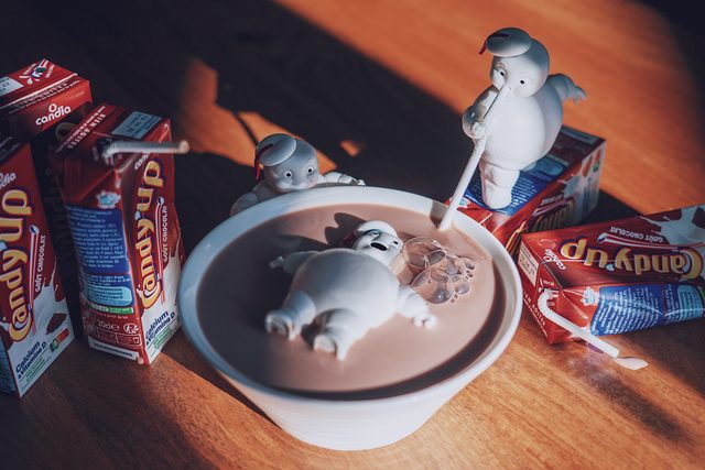 Small marshmallow men bathing in a bowl of hot chocolate, surrounded by chocolate milk cartons