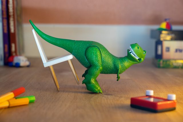 Rex, the green toy dinosaur, pulling up a tiny white chair on a desk